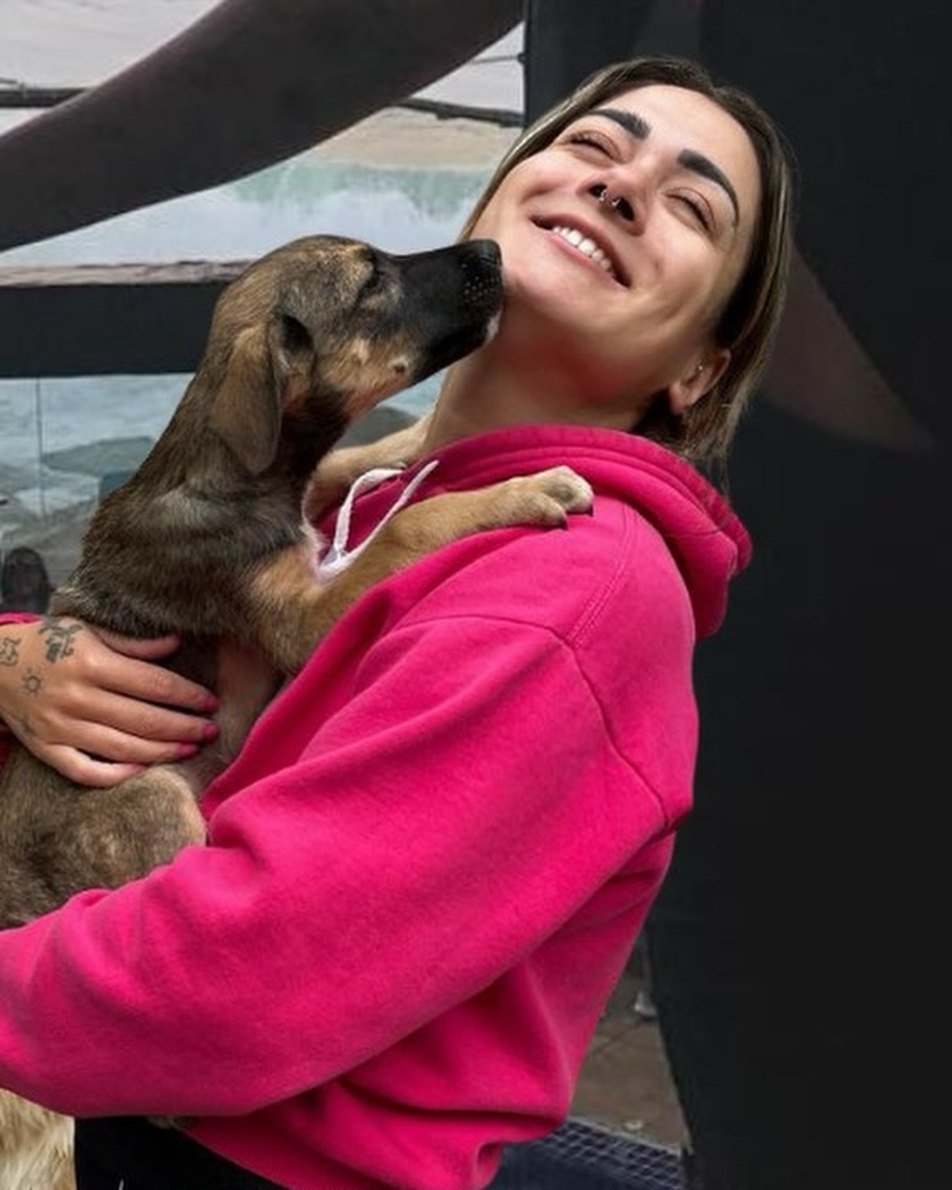 Babi sorrindo com um cachorrinho no colo que lambe o rosto dela